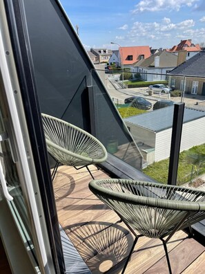 Ein Balkon mit zwei Korbstühlen, einem Holzboden und Blick auf Wohngebäude.