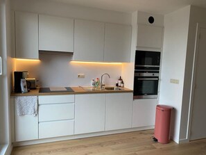 Eine moderne Küche mit weißen Schränken, einer Holzarbeitsplatte, einem Spülbecken, einer Kaffeemaschine und einem Backofen.