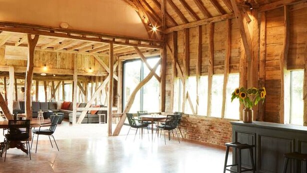 A spacious interior with high ceilings, exposed wooden beams, and a central seating area with tables and chairs.