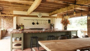 A rustic kitchen with a large island, hanging pots, and a clock on the wall.