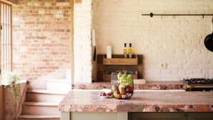 A kitchen with a marble countertop, a brick wall, and a wooden shelf with bottles.