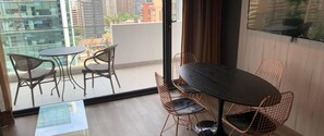 A balcony with a round table and four chairs, a glass door, and a view of buildings. - Santiago Retreat EXC | Modern 1 BR apartment in Las Condes (Santiago)