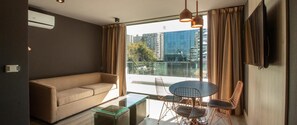 Ein modernes Wohnzimmer mit einer Couch, einem Glastisch, einem Esstisch mit Stühlen und einem großen Fenster mit Vorhängen.