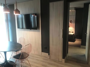 Ein modernes Zimmer mit Holzboden, einem runden Tisch mit Stuhl, einem flachbildfernseher an der Wand und einer Tür zu einem anderen Raum.