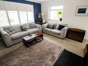 A living room with two sofas, a coffee table, a rug, a lamp, a window, and a framed picture on the wall. - 4 Cardell Way (Newquay)