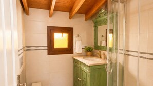 Un baño con techo de madera, tocador verde, cabina de ducha con paredes de vidrio y un inodoro blanco.