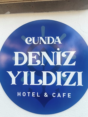 Ein rundes Schild mit dem Text 'CUNDA DENİZ YILDIZI HOTEL & CAFE' auf weißem Grund.