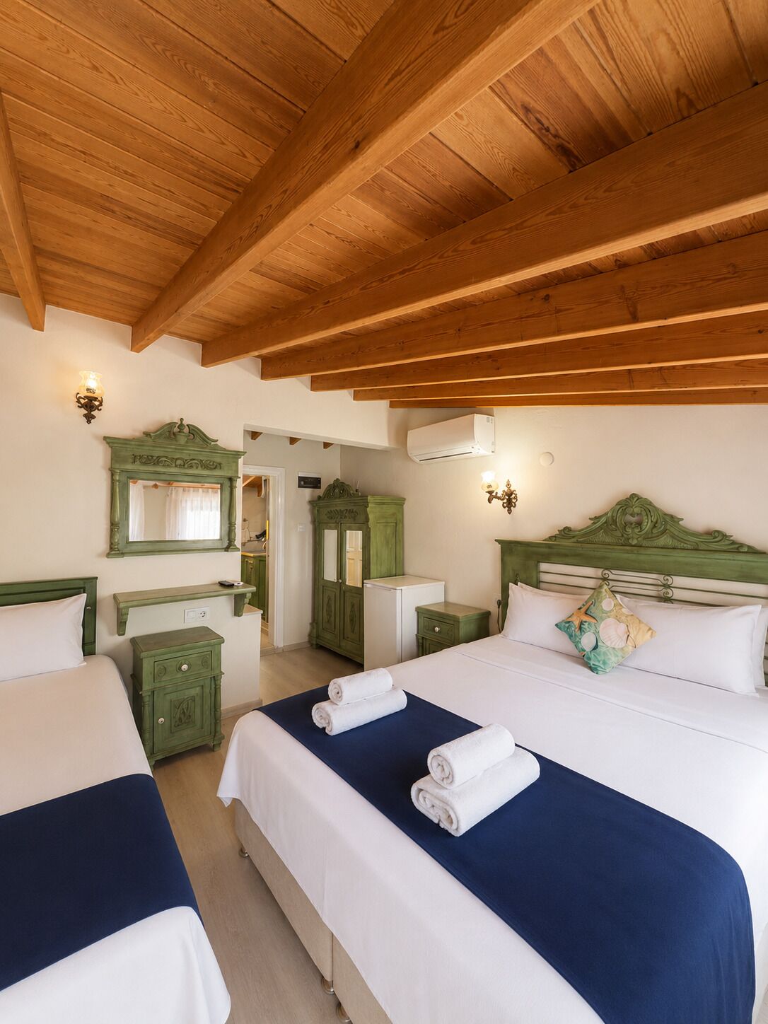 Ein Hotelzimmer mit zwei Betten, Holzbalkendecke, einem grünen Schminktisch und einem Spiegel.