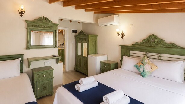 Habitación de hotel con dos camas, vigas de madera en el techo, tocador verde y un espejo.