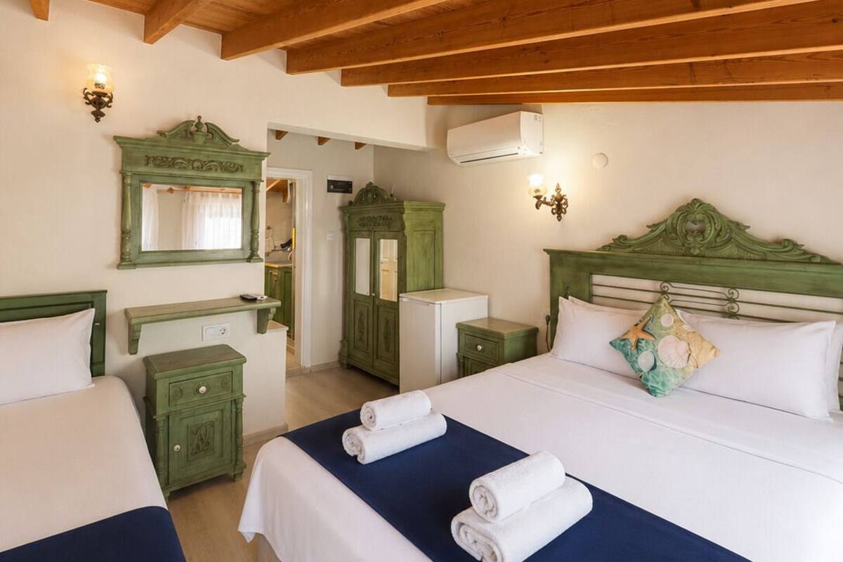 Une chambre d’hôtel avec deux lits, des poutres apparentes en bois au plafond, une coiffeuse verte et un miroir.