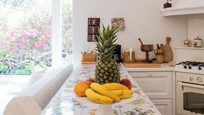 A kitchen with a fruit display, a stove, and a window with a view of pink flowers. - Bouganville by IschiaExp (Ischia Porto)