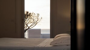 A bedroom with a bed, pillows, and a view of the sea through an open door. - Bouganville by IschiaExp (Ischia Porto)