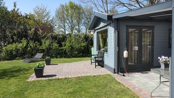 A modern house with a patio, a chair, a table, and a garden.