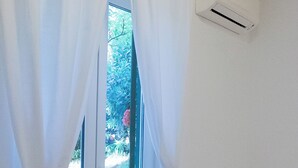 Quarto com porta de vidro deslizante, cortinas brancas, ar condicionado branco e sofá branco.