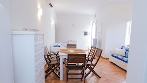 Uma área de refeições com uma mesa branca, cadeiras de madeira e um armário branco.