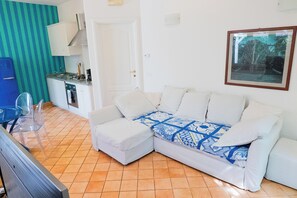 A compact living space with a kitchenette, a white sofa with patterned cushions, and a framed picture on the wall. - Il Gelso Nero by IschiaExp (Ischia Porto)