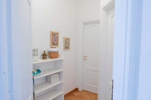 A narrow hallway with a white door, a shelf with decorative items, and a tiled floor. - Il Gelso Nero by IschiaExp (Ischia Porto)