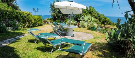An outdoor seating area with a table and chairs, surrounded by greenery and a view of the ocean.