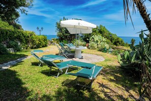 An outdoor seating area with a table and chairs, surrounded by greenery and a view of the ocean. - Il Gelso Nero by IschiaExp (Ischia Porto)