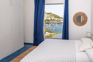 Ein Schlafzimmer mit Bett, Blick auf Boote und eine Küstenstadt, einem runden Spiegel und einem Kleiderschrank.