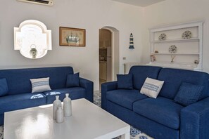 Ein Wohnzimmer mit zwei blauen Sofas, einem weißen Couchtisch und einer weißen Vitrine mit dekorativen Tellern.