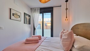 Ein ordentlich bezogenes Bett mit rosa Bettwäsche, ein großes Fenster mit Blick auf Gebäude und Kunstwerke an der Wand.