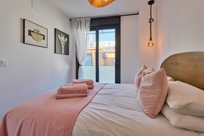 Ein ordentlich bezogenes Bett mit rosa Bettwäsche, ein großes Fenster mit Blick auf Gebäude und Kunstwerke an der Wand.