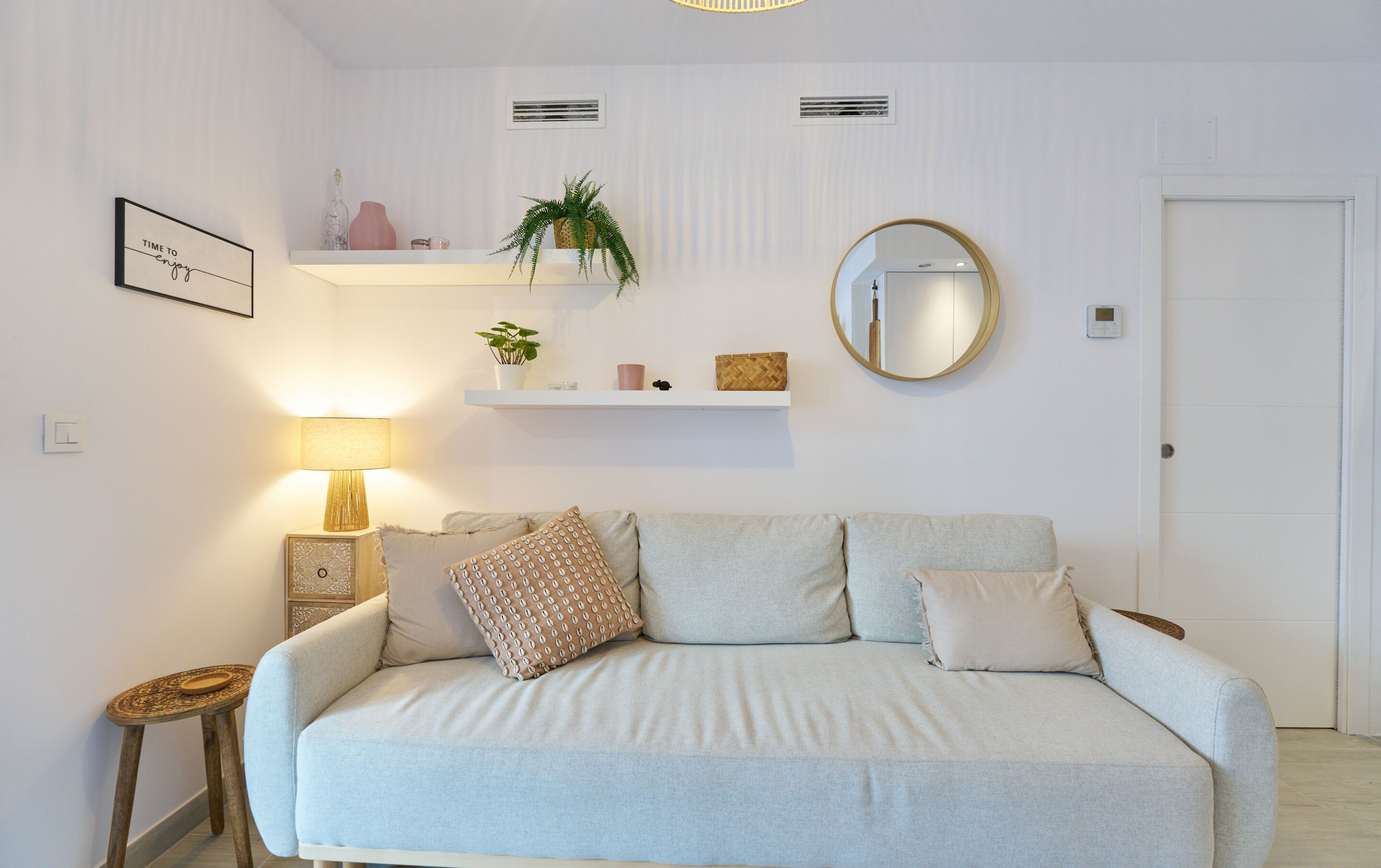 A modern living room with a sofa, a side table, a lamp, a mirror, and wall-mounted shelves with decorative items.