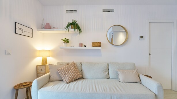 Ein modernes Wohnzimmer mit einer Couch, einem Beistelltisch, einer Lampe, einem Spiegel und Wandregalen mit Dekoration.