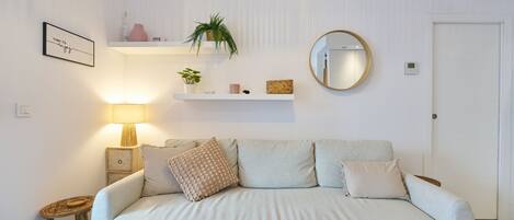 A modern living room with a sofa, a side table, a lamp, a mirror, and wall-mounted shelves with decorative items.