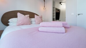 Ein ordentlich bezogenes Bett mit rosa Bettwäsche und Kissen, ein Holz-Kopfteil und eine hängende Leuchte.