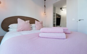 Ein ordentlich bezogenes Bett mit rosa Bettwäsche und Kissen, ein Holz-Kopfteil und eine hängende Leuchte.