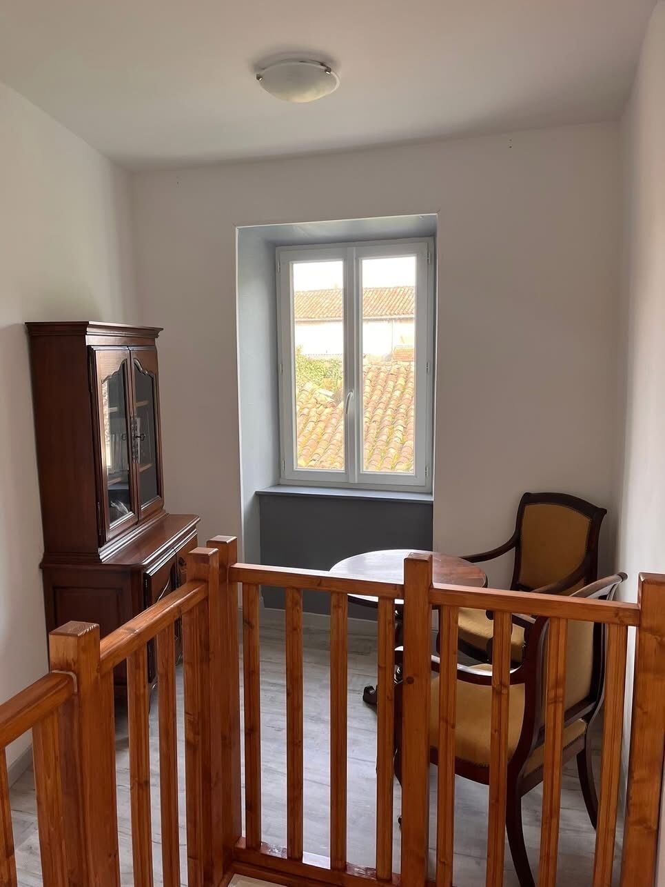 Ein Zimmer mit Holztisch, Stühlen, einem Schrank und einem Fenster mit Blick auf Gebäude.