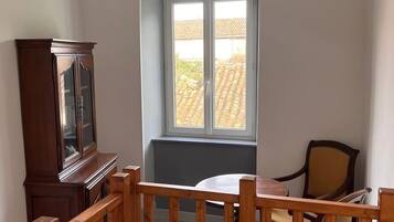 Ein Zimmer mit Holztisch, Stühlen, einem Schrank und einem Fenster mit Blick auf Gebäude.