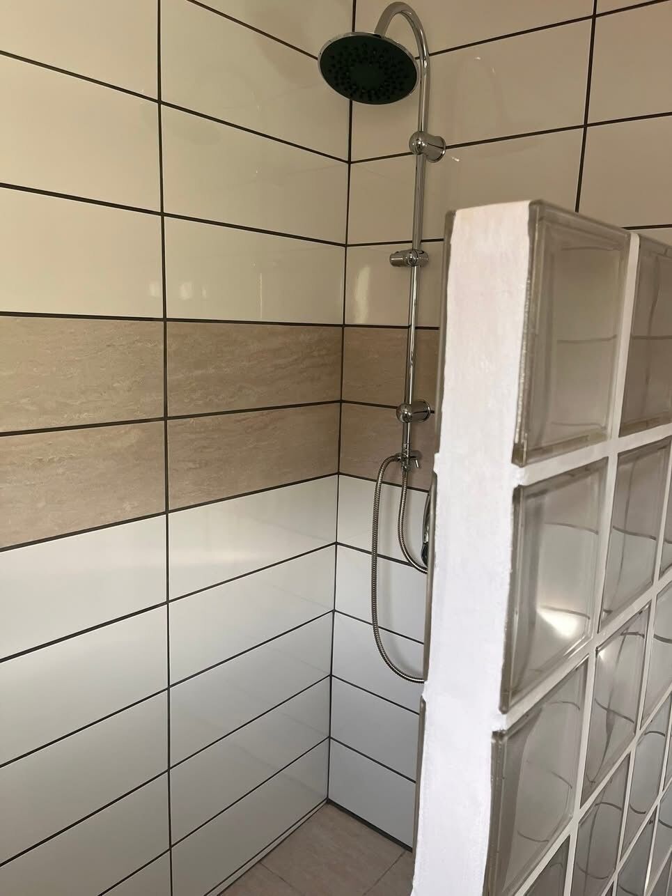 A shower with a handheld showerhead, a wall-mounted control, and a glass door.