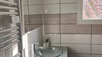 Ett badrum med ett handfat i glas, vita kakelplattor, en handdukshängare och ett fönster med utsikt.
