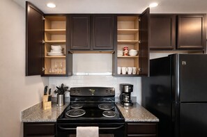 A kitchen with dark cabinets, a black refrigerator, a stove, and a coffee maker. - Designer UAB Condo | King Bed | Balcony View D2 (Birmingham)