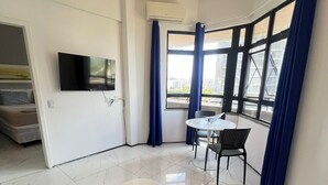Ein modernes Wohnzimmer mit einer Couch, zwei kleinen Tischen, einem Fernseher und einem großen Fenster mit Vorhängen.