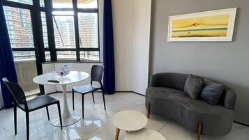 Uma sala de estar moderna com um sofá cinzento, duas mesas redondas e um quadro na parede.