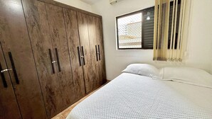 Une chambre dotée d’une grande armoire, d’un lit avec une literie blanche et d’une fenêtre avec des stores.