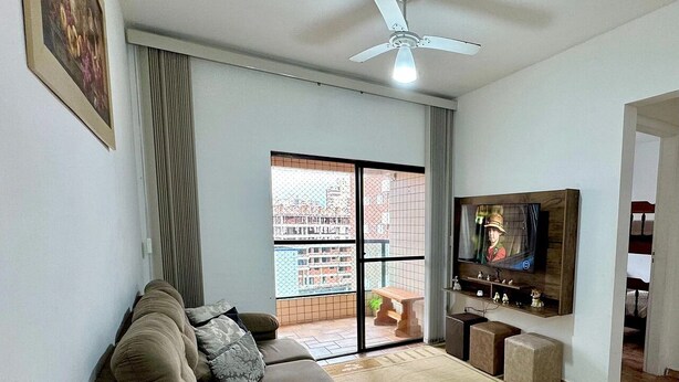 Un salon comprenant un canapé, un téléviseur, un ventilateur de plafond et une porte-fenêtre coulissante donnant sur un balcon.