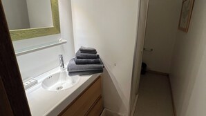 Un baño con lavamanos blanco, espejo y una pila de toallas.