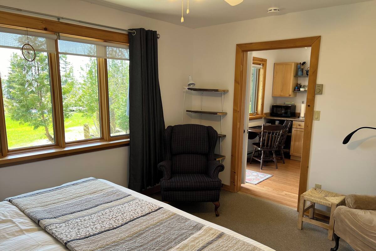 A bedroom with a bed, a chair, a desk, and a view of the outdoors.