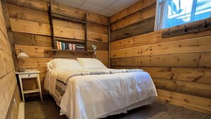 Una habitación de cabaña de madera con cama, mesita de noche, lámpara y estanterías.