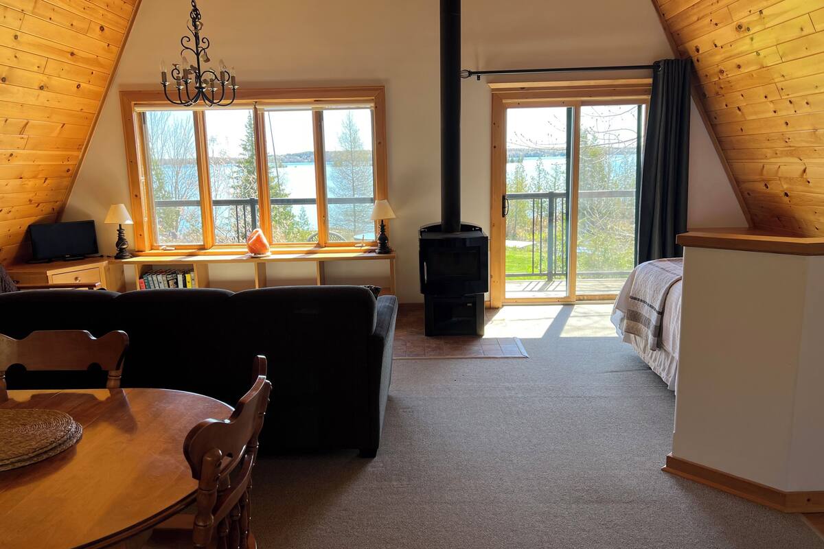 A cozy loft bedroom with a wooden ceiling, a fireplace, a bed, a desk, and a dining area.