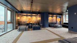 Un amplio salón con grandes ventanales, un techo alto y un mural de un barco velero.