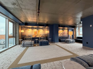 A spacious lounge with large windows, a high ceiling, and a mural of a sailing ship. - Hôtel Corbin (Québec)