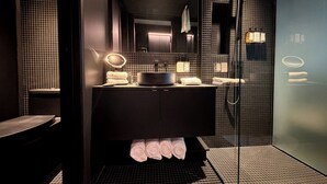 Un baño moderno con tocador negro, espejo, lavabo, ducha y toallero.