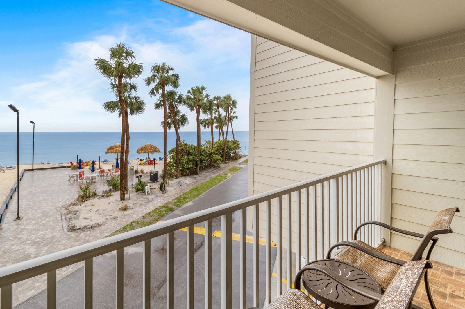 Een balkon met uitzicht op een strand, palmbomen en een heldere lucht.