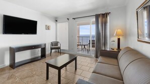 Sala de estar con televisor, sofá, mesa, silla, balcón con vistas y lámpara.